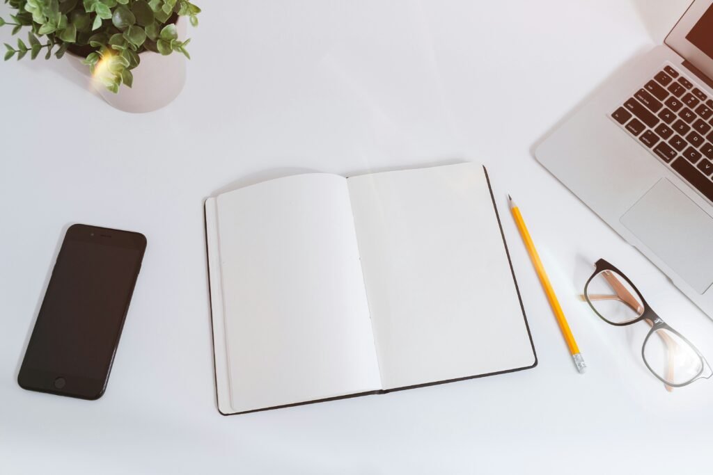 imagen de una libreta en blanco, lápiz, celular y lentes